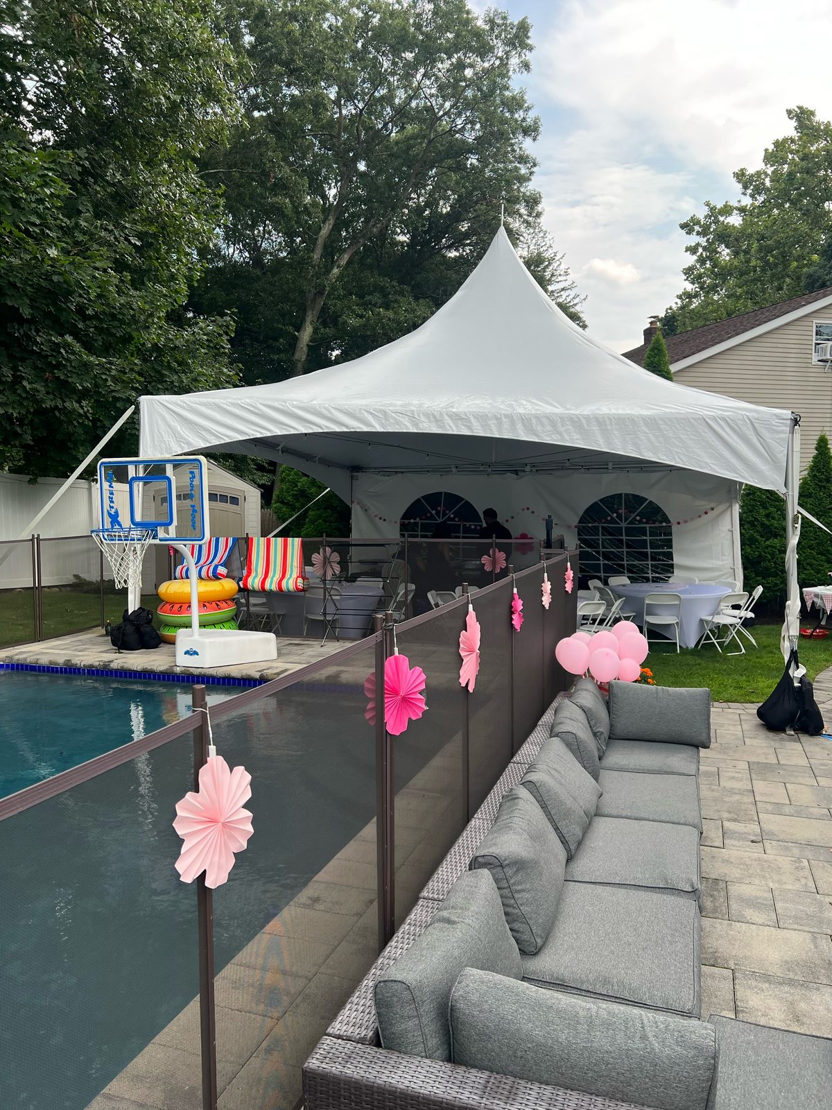 High peak tent with window sidewalls decorated for a girl's birthday party with pink balloons and paper fans beside a backyard pool