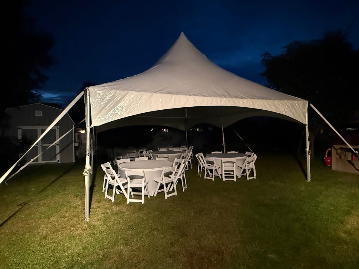 High peak tent glowing at dusk with round tables and white folding chairs set for an evening party