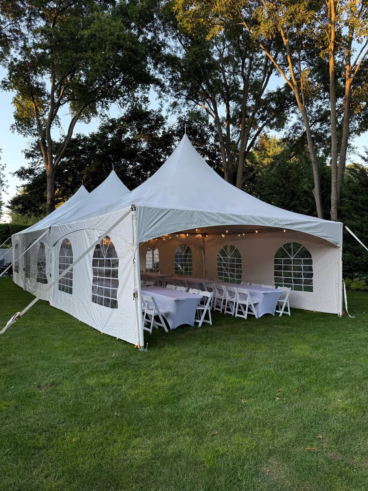 White high peak party tent with string lights and tables set for guests in a Long Island backyard