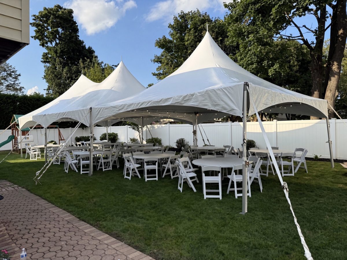 Multi-peak tent with string lights over round tables and white chairs in a fenced Long Island backyard